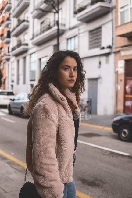 Ernste junge Frau mit lockigem Haar, die in die Kamera schaut, während sie auf der Straße steht — Stockfoto
