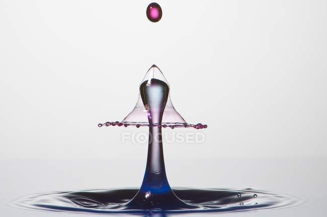 Close-up de respingo de líquido transparente de cor no fundo cinza — Fotografia de Stock