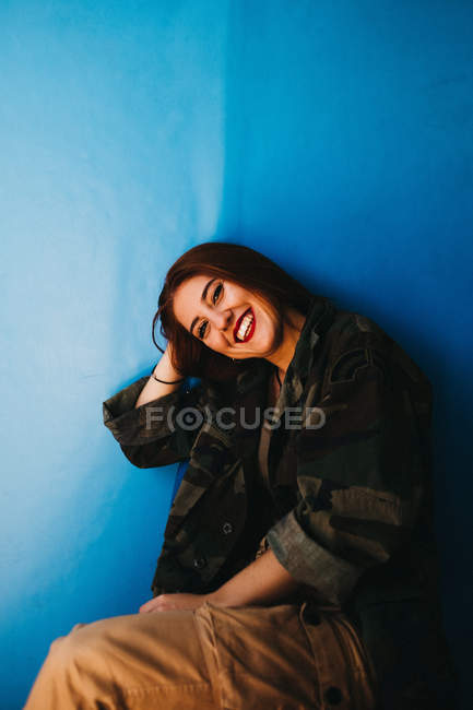 Усміхнена приваблива жінка тримає голову біля синьої стіни — стокове фото