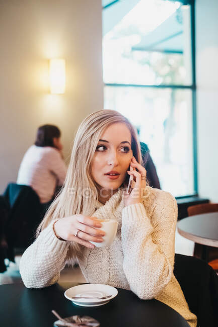 Donna che parla smartphone a tavola con tazza di bevanda — Foto stock