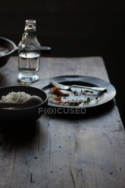 Ciotola di riso e piatto vuoto su tavolo in legno rustico su sfondo scuro — Foto stock