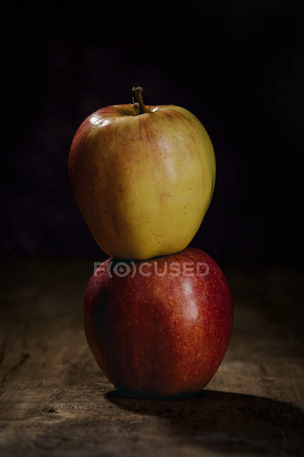 Stacked red and yellow fresh apples on wooden table on dark background — Stock Photo