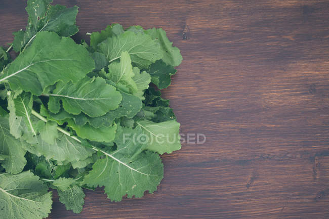 Green vegetable leaves on brown wooden surface — Stock Photo