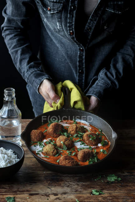 Manos humanas sosteniendo sartén pesada de coliflor deliciosa y bolas de quinua con salsa y perejil sobre la mesa de madera - foto de stock
