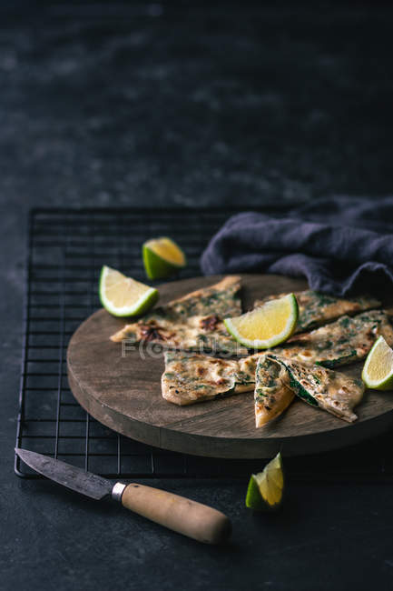 Slices of fresh lime and pieces of gozleme on wooden board in dark room — Stock Photo