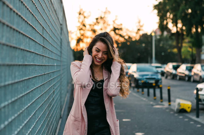 Сміється молода жінка, що йде вулицею біля автомобілів на заході сонця — стокове фото
