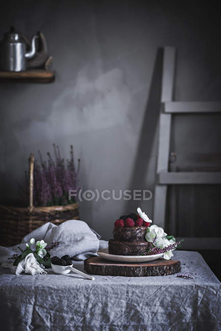 Chocolate cake decorated with raspberries and flowers served on plate on wooden stand — Stock Photo