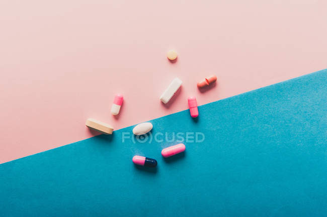 Pilules et capsules dispersées sur fond bleu et rose — Photo de stock