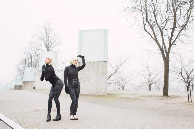 Attractive young women in dark wear posing on street near trees in Lithuania — Stock Photo
