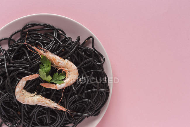 Schwarze Pasta mit Garnelen auf Teller auf rosa Hintergrund serviert — Stockfoto