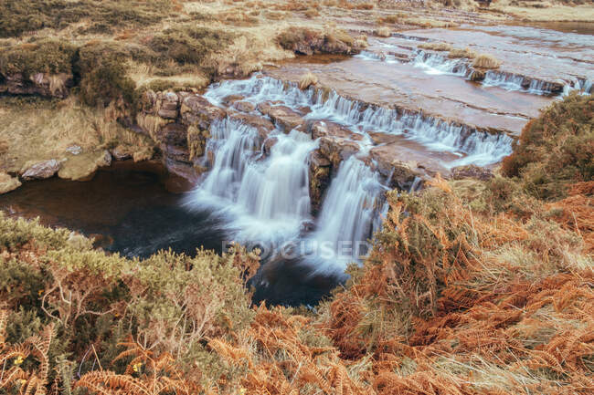 Landschaft von Wasserfällen in Langzeitbelichtung, die von einer Felsklippe in trockenes herbstliches Gras fallen, Spanien — Stockfoto