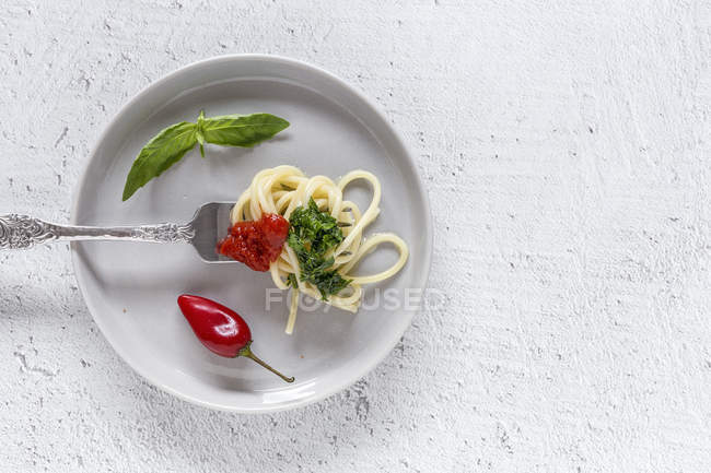 Espaguete com molho de tomate e pesto na placa no fundo branco — Fotografia de Stock