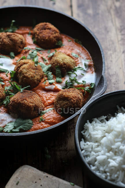 Pan with cauliflower and quinoa balls in sauce and bowl of rice on wooden table — Stock Photo