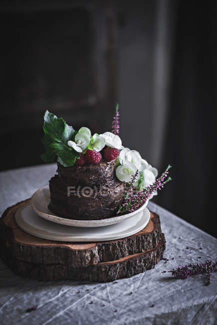 Шоколадний торт, прикрашений малиною та квітами, поданими на тарілці на дерев'яній підставці — стокове фото