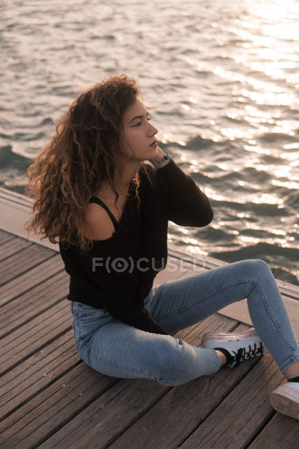 Affascinante giovane donna seduta sul molo di legno vicino all'acqua — Foto stock