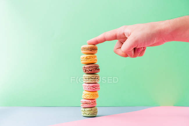 Mano della persona con dito mostrante su mucchio di macarons gustosi freschi su bordo blu su sfondo verde — Foto stock