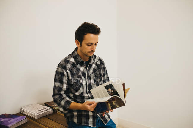 Молодий чоловік тримає журнал біля столу в кімнаті — стокове фото