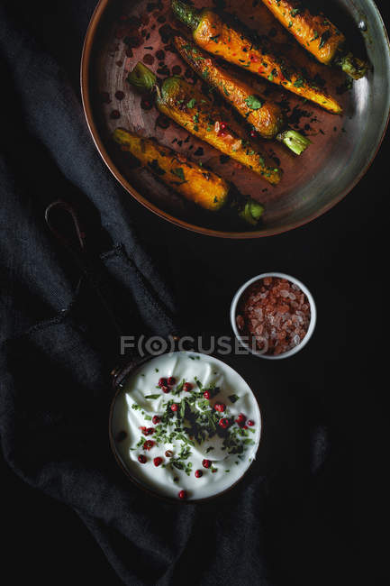Healthy roasted carrots with herbs and spices on black fabric with sauce — Stock Photo