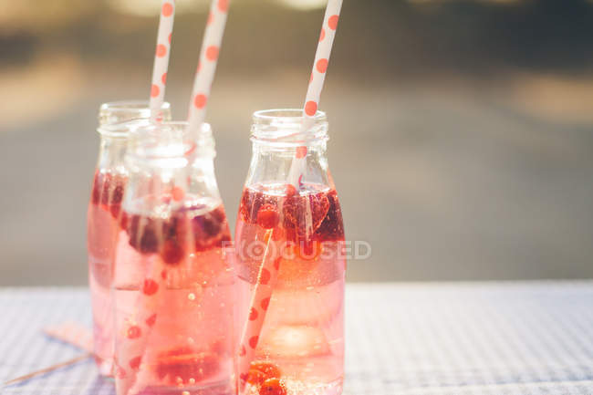 Botellas con bebida de fruta fresca y pajitas para beber en la mesa al aire libre - foto de stock
