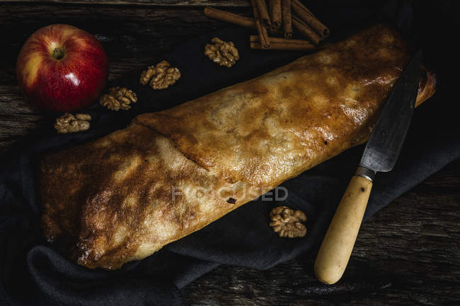 Homemade apple strudel with nuts, raisins and cinnamon on dark wood background — Stock Photo