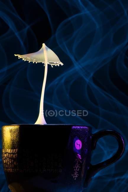 Крупним планом знімок сплеск жовтої рідини над азіатською чашкою і чорним тлом — стокове фото