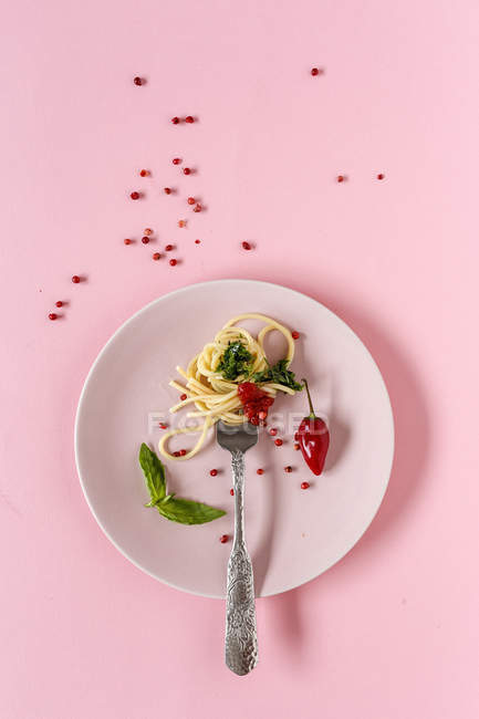 Spaghetti with tomato and pesto sauce on plate on pink background — Stock Photo