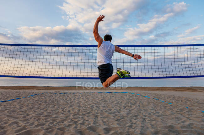 Back view of man in sportswear jumping high near volleyball net during outdoor workout on beach — Stock Photo