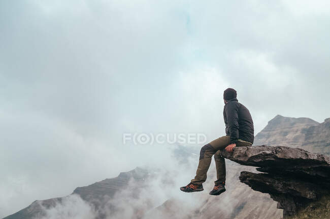 Homme assis sur le rocher près de la montagne entre les nuages — Photo de stock