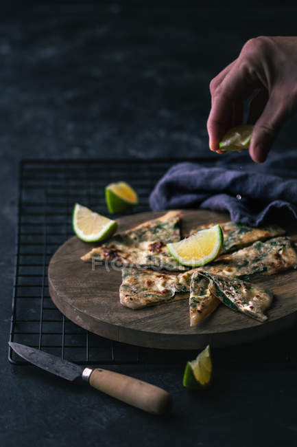 Hand of anonymous person squeezing fresh lime on slices of gozleme on wooden board — Stock Photo