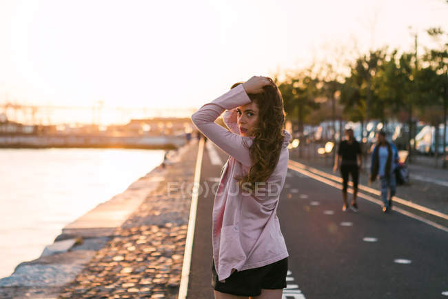 Jovem mulher andando no calçadão perto de água e beco ao pôr do sol — Fotografia de Stock
