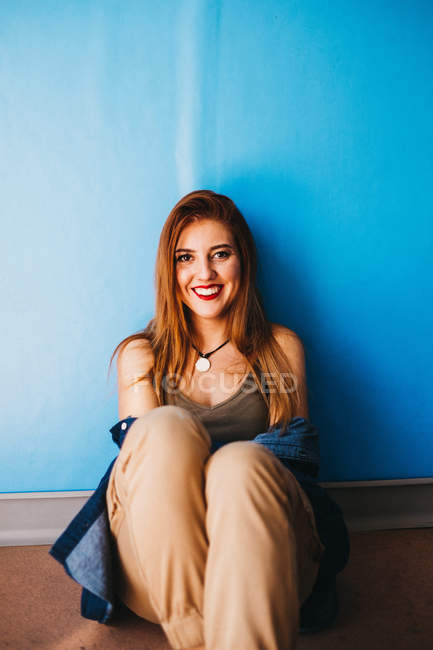 Belle femme assise près du mur bleu — Photo de stock