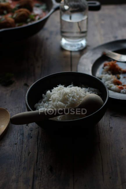 Миска рису і порожня тарілка на сільському дерев'яному столі на темному фоні — стокове фото