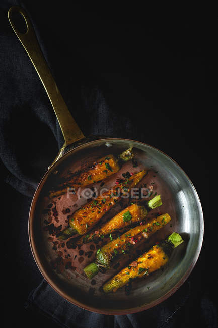 Healthy roasted carrots with herbs and spices in frying pan on black background — Stock Photo
