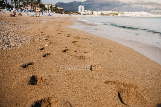 Huellas de pies humanos sobre arena mojada cerca del mar ondulante en Altea, España - foto de stock