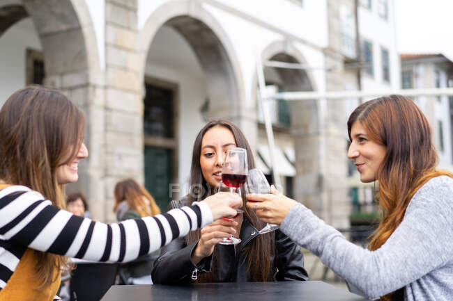Senhoras sorridentes atraentes que batem copos de vinho à mesa de café de rua no Porto, Portugal — Fotografia de Stock