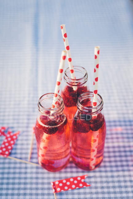 Bottles with fresh fruit drink and drinking straws on checkered tablecloth — Stock Photo