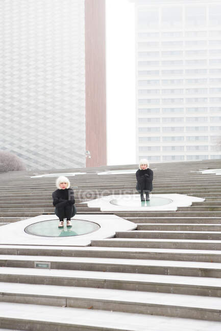 Blond ladies in same cloths sitting on steps near buildings — Stock Photo