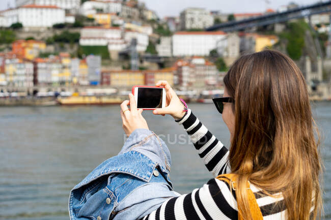 Woman taking photo of river on smartphone from bridge — Stock Photo