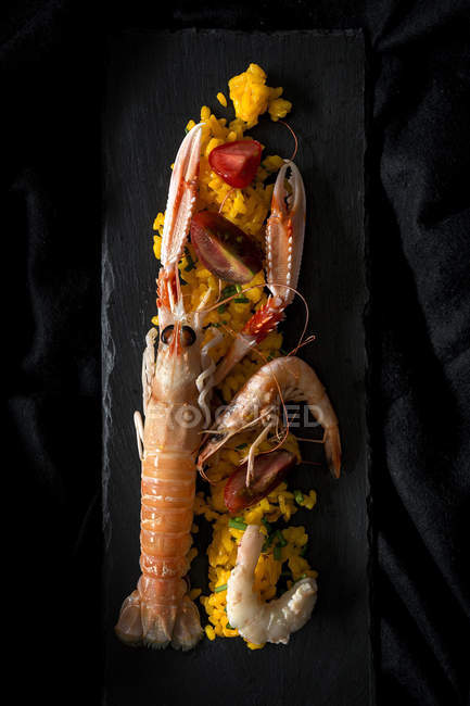 Paella casera con cangrejos de río y gambas servidas en pizarra sobre tela negra - foto de stock