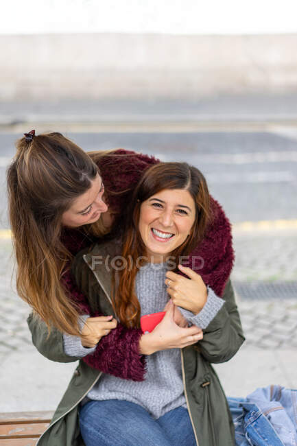 Señora abrazando desde atrás alegre joven atractiva mujer - foto de stock