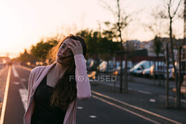 Jeune fille avec la main dans les cheveux marchant sur l'allée au coucher du soleil — Photo de stock