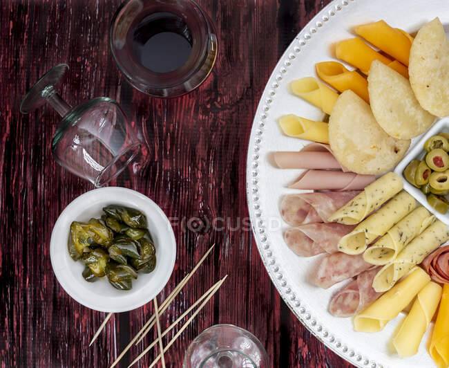 Vue de dessus de la plaque avec du fromage tranché et des saucisses et des verres à vin placés près sur un fond en bois — Photo de stock
