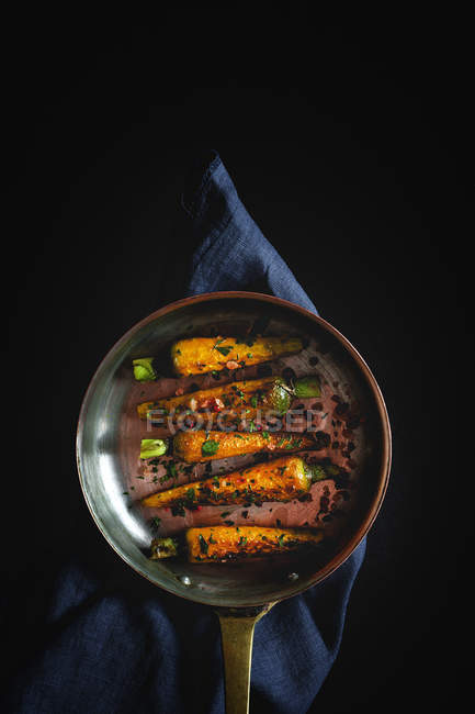 Gesunde geröstete Karotten mit Kräutern und Gewürzen in der Pfanne auf schwarzem Hintergrund — Stockfoto