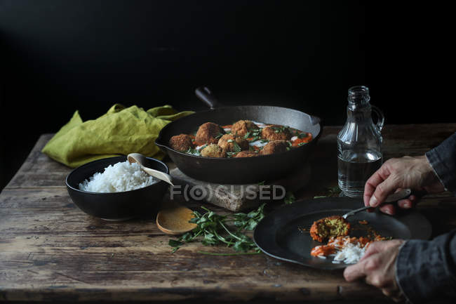 Manos de la persona que toma la coliflor y la bola de quinua con arroz del plato en la mesa de madera - foto de stock