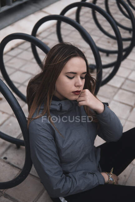 Charming woman in coat and leggins sitting near parking for bicycles — Stock Photo