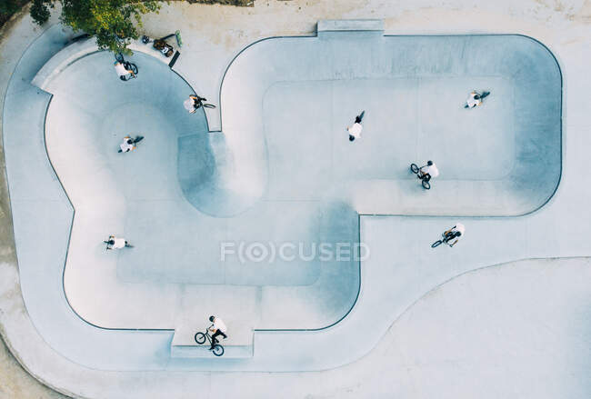 From above view of spacious skate park with group of men in white T-shirts doing tricks on BMX — Stock Photo