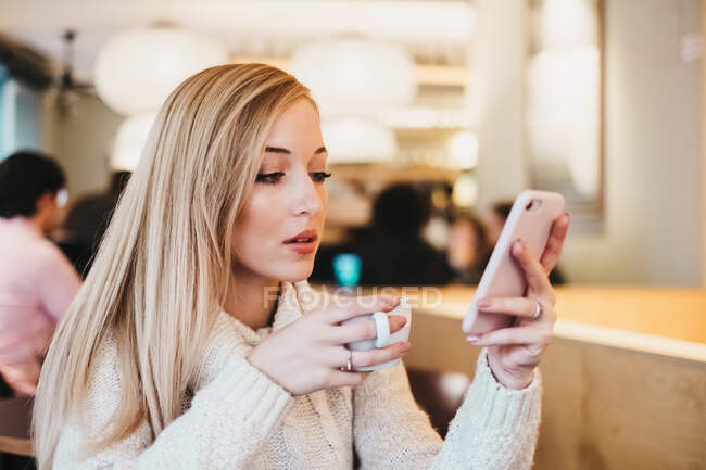 Femme utilisant un smartphone à table avec une tasse de boisson — Photo de stock