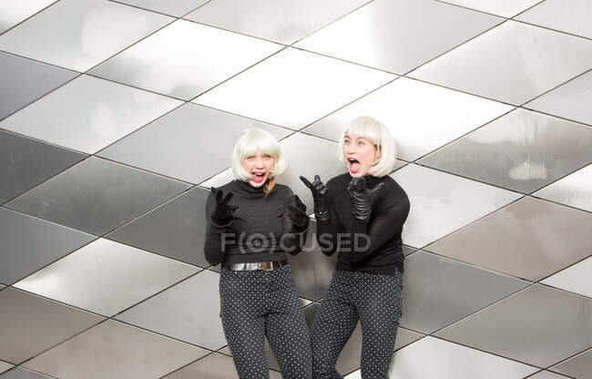 Rubia sonriente damas en los mismos paños posando cerca de la pared - foto de stock