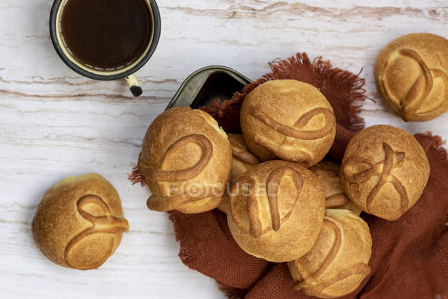 Fresh baked buns in heap on brown napkin on wooden table with cup of tea — Stock Photo