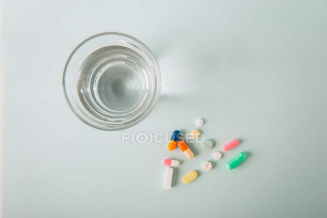 Різнокольорові таблеток і капсул розкидані зі склянкою води на білому тлі — стокове фото